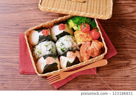 A bento box of rice balls, salmon, small sardines, pickled plums, fried chicken, tamagoyaki (Japanese omelette), broccoli, and cherry tomatoes. 123186831