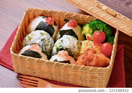 A bento box of rice balls, salmon, small sardines, pickled plums, fried chicken, tamagoyaki (Japanese omelette), broccoli, and cherry tomatoes. A bento box of rice balls, salmon, small sardines, pickled plums, fried chicken, tamagoyaki (Japanese omelette), broccoli, and cherry tomatoes. 123186832