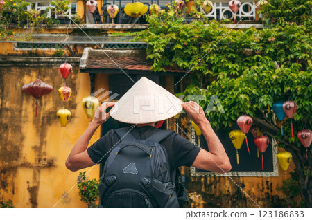 back of Asian male traveler tourist in traditional vietnamese hat on street in old town in Hoi An city in Vietnam in Asia 123186833