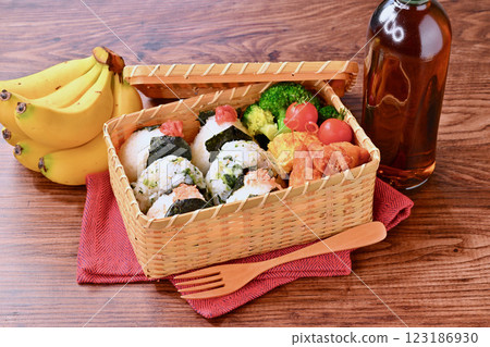 A bento box of rice balls, salmon, small sardines, pickled plums, fried chicken, tamagoyaki (Japanese omelette), broccoli, and cherry tomatoes. 123186930