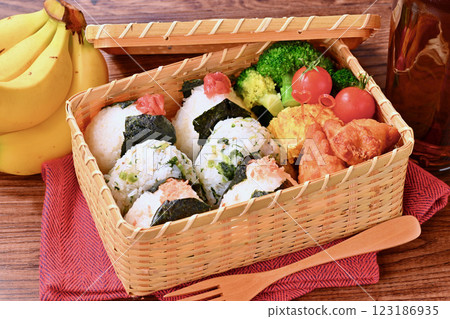 A bento box of rice balls, salmon, small sardines, pickled plums, fried chicken, tamagoyaki (Japanese omelette), broccoli, and cherry tomatoes. A bento box of rice balls, salmon, small sardines, pickled plums, fried chicken, tamagoyaki (Japanese omelette), broccoli, and cherry tomatoes. 123186935