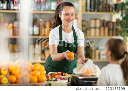 Buying ripe tangerines in store - female salesperson weighs tangerines on scales and hands them to teenage girl 123187109