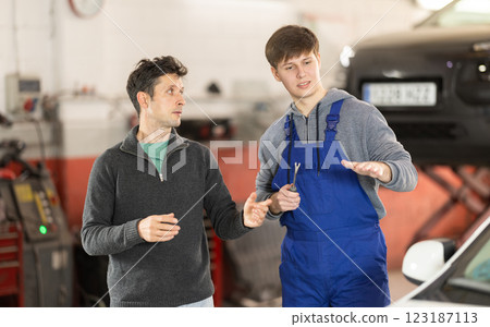 Young man car mechanic talks with man client in workshop and takes order. Young man car mechanic talks with man client in workshop and takes order. 123187113