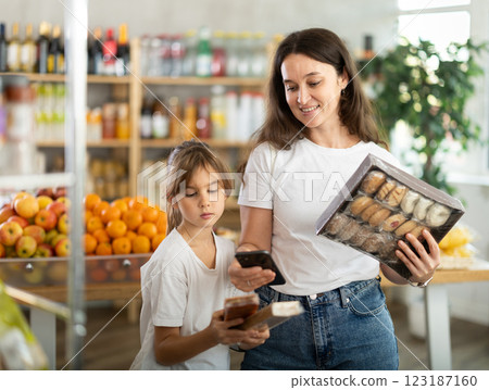 Girl with mother customers at shop scans QR code on sweets package using phone camera 123187160