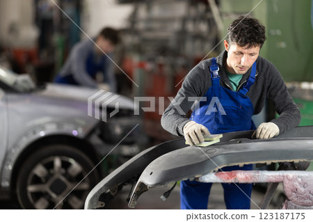 Car bumper repair in car service - professional car painter polishes and prepares bumper before painting 123187175