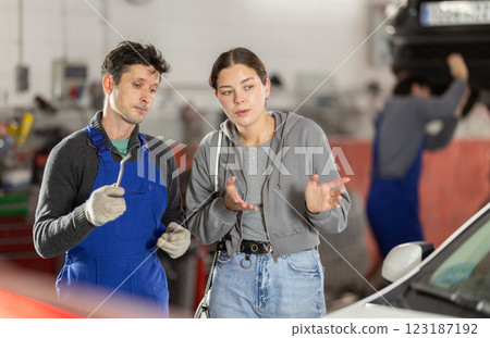 Male auto mechanic discussing with woman the cost and time to repair her car at car service Male auto mechanic discussing with woman the cost and time to repair her car at car service 123187192