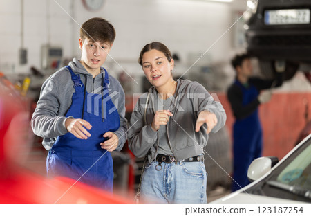 Young man car mechanic talks with girl client in workshop and takes order. 123187254