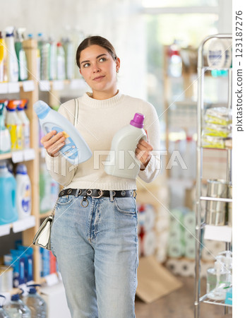 Girl housewife in household store examines package, chooses liquid detergent 123187276