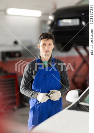 Adult man mechanic in uniform posing in car service station Adult man mechanic in uniform posing in car service station 123187385