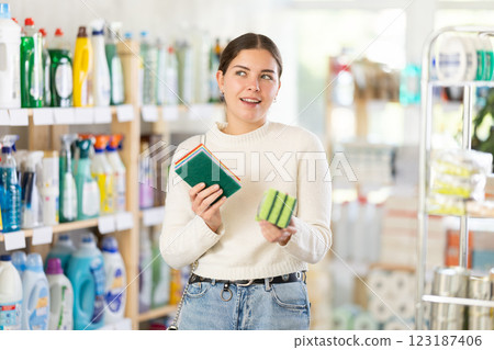Young woman housewife in household store examines package, chooses abrasive sponge Young woman housewife in household store examines package, chooses abrasive sponge 123187406