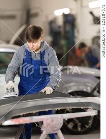 Young man auto mechanic polishes body parts by car buffer polisher machine tool 123187573