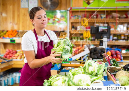 Supermarket female employee lays out cauliflower on shelves in greengrocery store 123187749