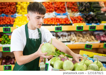 Focused male seller lay out round bottlegourd vegetable on counter in supermarket Focused male seller lay out round bottlegourd vegetable on counter in supermarket 123187821