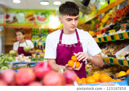 Hardworking young salesman puts fresh oranges on the counter Hardworking young salesman puts fresh oranges on the counter 123187858