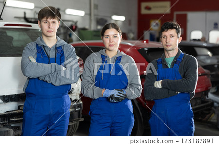 Team of auto mechanics, two men and one woman, wearing blue overalls and posing, ready to provide professional vehicle service Team of auto mechanics, two men and one woman, wearing blue overalls and posing, ready to provide professional vehicle service 123187891