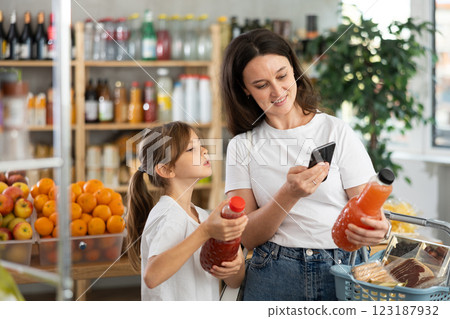 Girl with mother customers at shop scans QR code on juice package using phone camera Girl with mother customers at shop scans QR code on juice package using phone camera 123187932