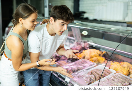 Spouse near butcher shop window inspects goods and choose sausages for grill 123187949