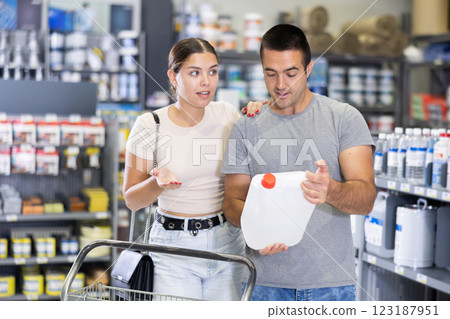 In store, husband with trolley and plastic canister in hands consults with wife about purchase paint In store, husband with trolley and plastic canister in hands consults with wife about purchase paint 123187951