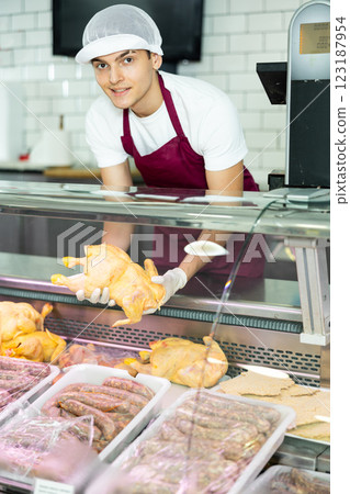 Positive young salesman demonstrating chicken in butcher shop 123187954