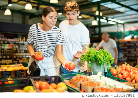 Young couple choosing ripe tomatoes in vegetable section of supermarket 123187991