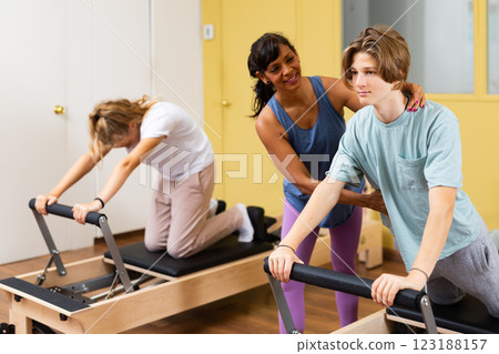 Femle instructor helps and monitors the difficulty of Pilates exercise for an boy Femle instructor helps and monitors the difficulty of Pilates exercise for an boy 123188157