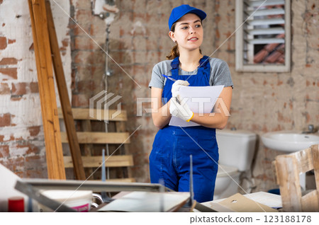 Female designer in blue overalls with papers planning building overhaul Female designer in blue overalls with papers planning building overhaul 123188178