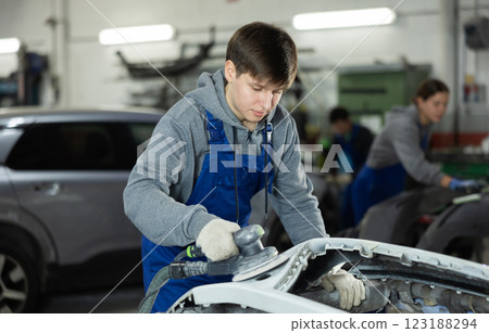Male mechanic prepares car for painting in workshop - using grinding machine he sands bumper before painting Male mechanic prepares car for painting in workshop - using grinding machine he sands bumper before painting 123188294