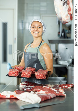 Saleswoman of butcher shop stands with tray and round blanks of ground beef, raw minced calf patties 123188347