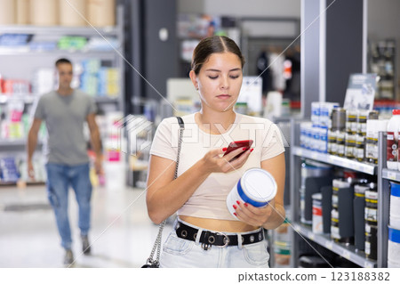 Woman examines product in paint shop and scans QR code on label of tin enamel dye 123188382