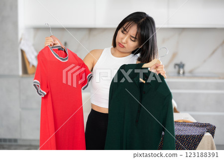 Sad young Asian girl trying to choose a dress in the kitchen 123188391