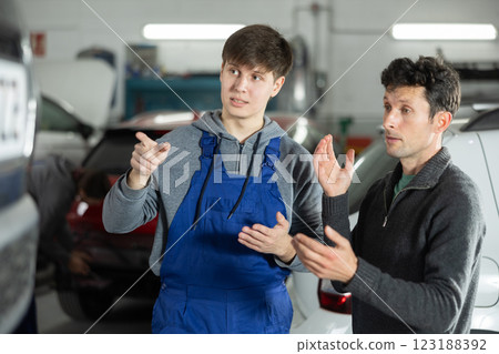 Adult car owner discusses with a young auto mechanic the cost and time of car repairs at car service center 123188392