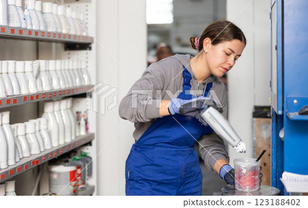 Girl colorist selects paint color by mixing different paint colors for subsequent painting of car in car service center 123188402