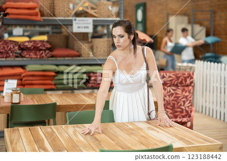 Thoughtful brunette choosing wooden patio table at garden center 123188442