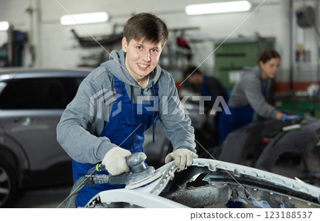 Young man auto mechanic polishes body parts by car buffer polisher machine tool Young man auto mechanic polishes body parts by car buffer polisher machine tool 123188537