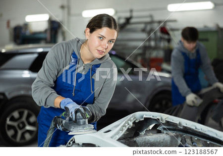 Young woman auto mechanic polishes body parts by car buffer polisher machine tool 123188567