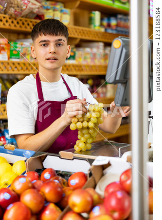 Focused european male seller weighing grape in supermarket 123188584