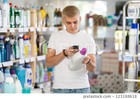 Positive young man buyer in shop holding and choosing detegrent, scan QR code 123188618