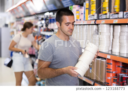 Skilled young handyman choosing painter tape in hardware store Skilled young handyman choosing painter tape in hardware store 123188773