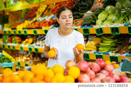 Happy smiling girl making purchases in supermarket, choosing fresh oranges 123188858