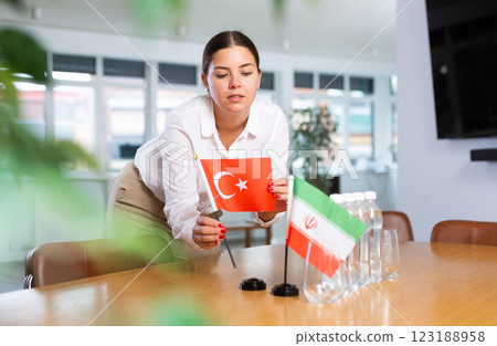 A woman in a white blouse with friendly smile arrangs flags of Turkey and Iran for meeting. A woman in a white blouse with friendly smile arrangs flags of Turkey and Iran for meeting. 123188958