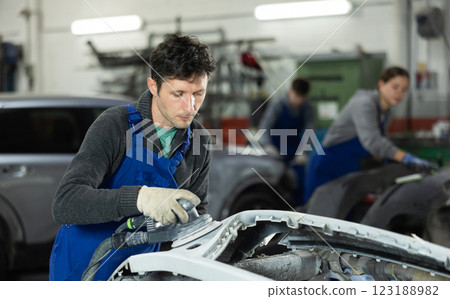 Man auto mechanic polishes body parts by car buffer polisher machine tool 123188982