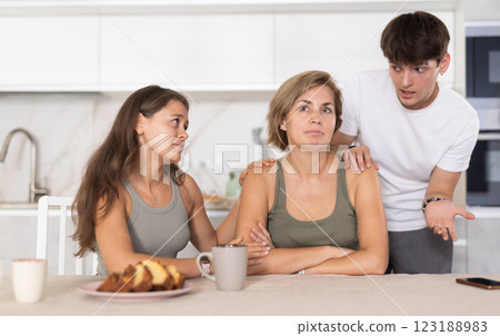 Sad mom sits silently in kitchen, adult children, guy and girl sympathize and comfort woman 123188983