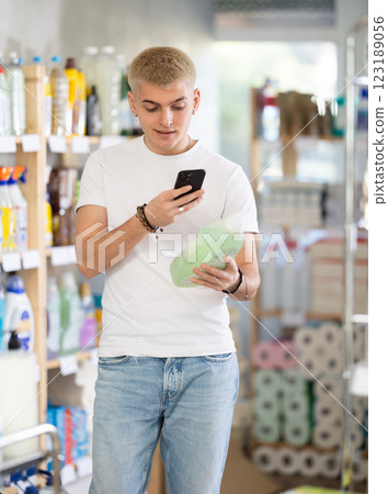 Positive young man buyer in shop holding and choosing detegrent, scan QR code 123189056