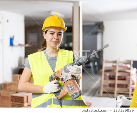 Young female builder standing with demolition hammer 123189089