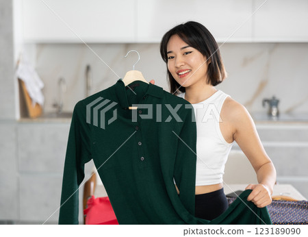 Happy young Asian girl trying to choose a dress in the kitchen Happy young Asian girl trying to choose a dress in the kitchen 123189090