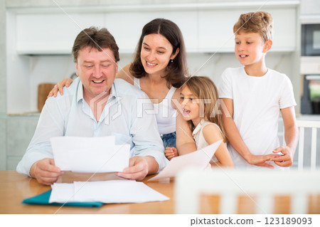 Joyful adult man reviewing documents at table with family 123189093
