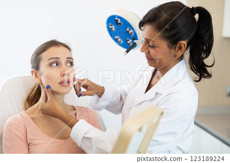 Cosmetologist examining face of young woman Cosmetologist examining face of young woman 123189224