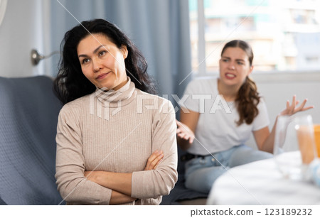 Upset woman sitting at home table with disgruntled woman behind Upset woman sitting at home table with disgruntled woman behind 123189232