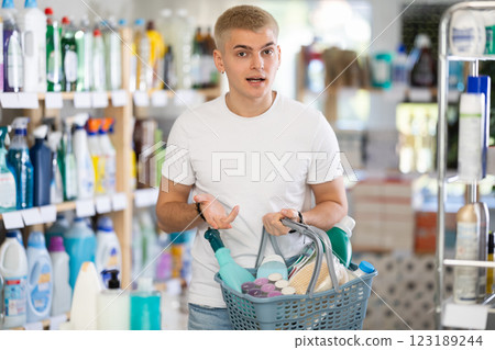 Portrait of young guy with full basket looking for something in supermarket 123189244