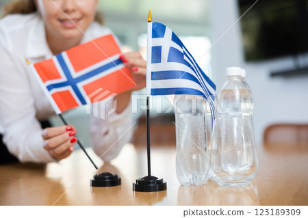 Unrecognizable girl sets midget flags of Greece and Norway before international negotiations 123189309